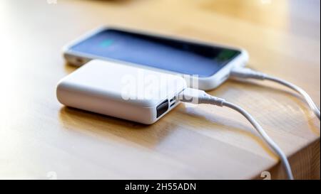 Ein Smartphone wird von einer kleinen weißen Powerbank geladen. Stockfoto