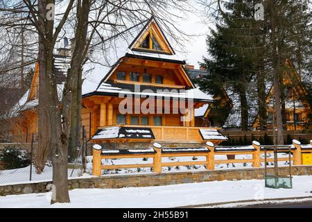 Zakopane, Polen - 21. März 2018: Während der Wintersaison ist in dem mit einem Holzzaun umzäunten Gebiet ein Blockhaus mit einem steilen Dach zu sehen. Stockfoto