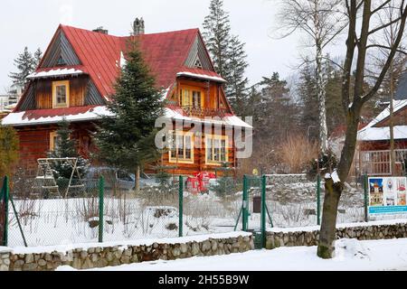 Zakopane, Polen - 21. März 2018: Eine Holzvilla mit einem steilen roten Dach ist an einem Wintertag auf einem eingezäunten Grundstück zu sehen. Stockfoto