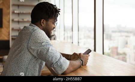 Lächelnder junger brasilianischer Ethnizitätsmann, der Handy benutzt Stockfoto