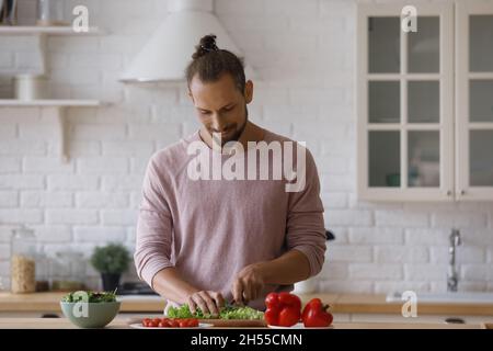 Lächelnder, hübscher junger Mann, der allein in der Küche kocht. Stockfoto
