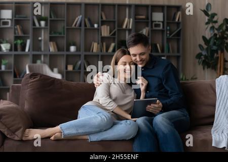 Ein glückliches Paar umarmt sich, benutzt ein Tablet und entspannt sich auf der Couch Stockfoto