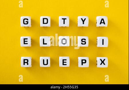 Weiße Würfel mit zufällig auf gelbem Hintergrund verstreuten Buchstaben Stockfoto