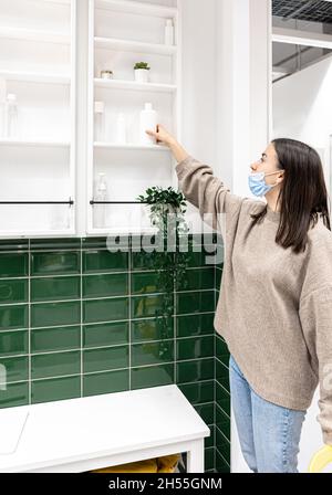 Junge Frau in einem Badezimmer mit grünen Fliesen und weißen Schränken an der Wand. Stockfoto