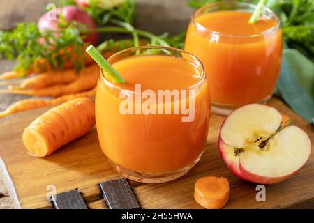 Frischer natürlicher Saft, gesundes Lebensmittelkonzept. Glas mit frischem Apfel- und Karottensaft auf einem rustikalen Holztisch. Stockfoto