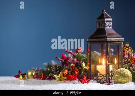 Brennende Weihnachtslaterne und Tannendekor in Schnee auf blauem Hintergrund mit Kopierraum Stockfoto