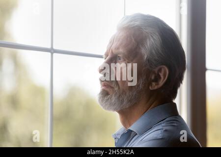 Besorgt besorgten älteren männlichen Rentner stehen allein durch das Fenster zu schauen Stockfoto