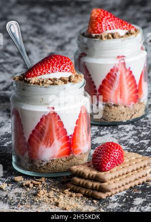 Zwei Gläser mit Joghurt, Erdbeeren und Keksen auf einem Holzbrett. Köstliches Dessert Stockfoto