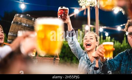 Fröhliche Frau, die mit Freunden in der Brauerei-Bar im Restaurant auf der Terrasse klirrend und kröckend Bier trinkt - Lifestyle- und Getränkekonzept mit jungen Leuten, die Spaß haben Stockfoto