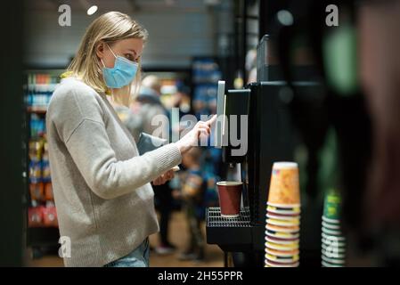 Frau in Maske mit Kaffeeautomaten. Stockfoto