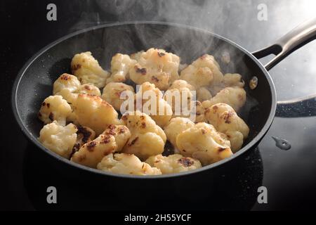 Dampfend geröstete Blumenkohlröschen in einer schwarzen Bratpfanne, Kochen von Gemüse für ein gesundes vegetarisches Gericht, ausgewählter Fokus, enge Schärfentiefe Stockfoto