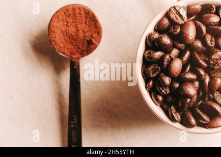 Draufsicht, Makroaufnahme einer Kaffeetasse voller Kaffeebohnen und Kaffeepulver in einem winzigen Löffel Stockfoto