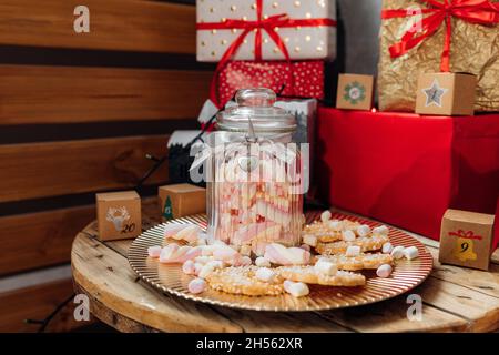 Weihnachtskekse rund. Zucker bestreut liegt auf Goldplatte auf dem Tisch neben Glas mit Marshallows gefüllt. Weihnachtsdekor, Weihnachtsgeschenke, Hap Stockfoto