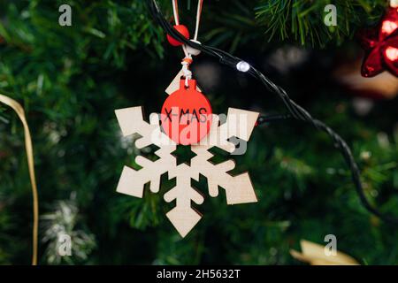 Konzept der Dekoration Weihnachtsbaum aus Öko-Materialien, große hölzerne Schneeflocke mit Inschrift zu Weihnachten hängt auf Ast von Fichte oder Kiefer am Stockfoto