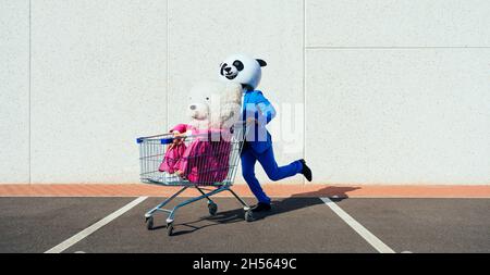 Ein erzähltes Bild eines Paares, das einen riesigen Pandakopf und farbige Anzüge trägt. Mann und Frau feiern auf einem Parkplatz. Stockfoto