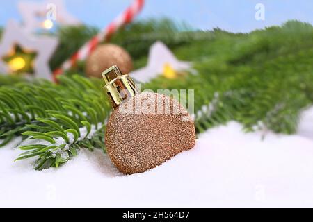Großes glitzerndes goldenes Spielzeug im Schnee mit grünen Fichtenzweigen und weißen Sternen mit Licht auf blauem Hintergrund. Weihnachten, Neujahr. Speicherplatz kopieren Stockfoto
