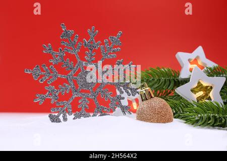 Silberne glitzernde Schneeflocke mit Sternlaternen und grünen Fichtenzweigen und glänzenden Kugeln auf rotem Hintergrund. Weihnachten, Neujahr. Speicherplatz kopieren Stockfoto