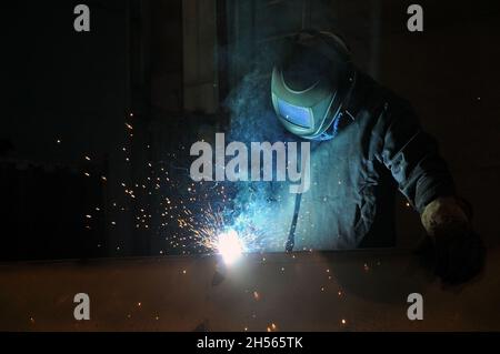 Elektrischer Schweißer bei der Arbeit. Ein Arbeiter schweißt Metallkonstruktionen in einer Fabrik. Berufe. Stockfoto