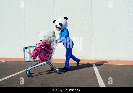 Ein erzähltes Bild eines Paares, das einen riesigen Pandakopf und farbige Anzüge trägt. Mann und Frau feiern auf einem Parkplatz. Stockfoto