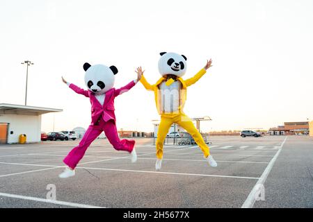 Ein erzähltes Bild eines Paares, das einen riesigen Pandakopf und farbige Anzüge trägt. Mann und Frau feiern auf einem Parkplatz. Stockfoto