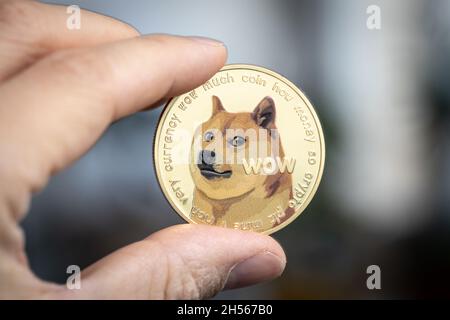 Dogecoin Kryptowährung physische Münze zwischen zwei Fingern gehalten Stockfoto