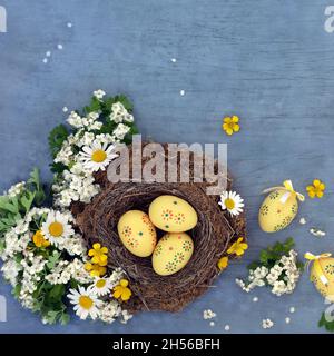 Abstrakte Komposition der Ostereierjagd mit verzierten Eiern, natürlichem Vogelnest, Butterblumen, Gänseblümchen und Weißdornblüten. Stockfoto