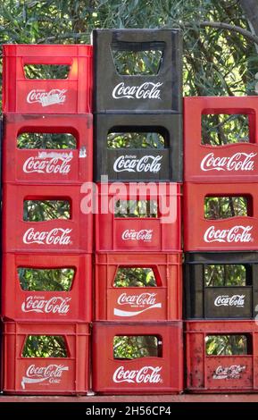 Almuñécar, Spanien; 28. Oktober 2021: Rote und schwarze Coca-Cola-Boxen, die sich draußen neben Bouganvillablumen stapeln Stockfoto