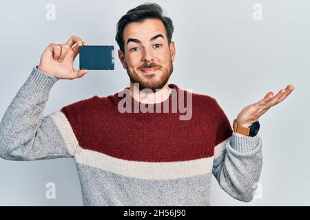 Hübscher kaukasischer Mann mit Bart, der SSD-Speicher hält, feiert Erfolge mit glücklichem Lächeln und mit erhobener Hand Stockfoto