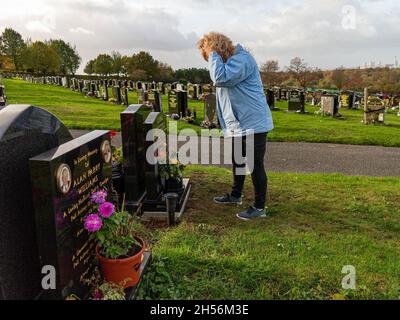 Aufgeregte Dame legt die Hände auf den Kopf, während sie am Grab der Eltern steht Stockfoto