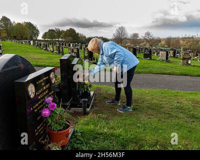 Reife Dame legt an einem sonnigen, aber windigen Tag Rosen auf ein Grab Stockfoto
