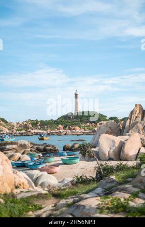 Landschaftlich schöner Blick auf den Leuchtturm an der schönen Küste mit großen Steinen. Blick auf die Bucht mit kristallklarem Wasser. Bunte vietnamesische Fischerboote. Stockfoto