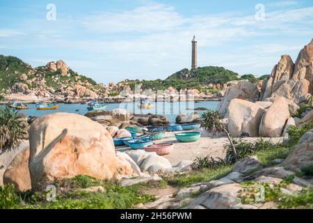 Landschaftlich schöner Blick auf den Leuchtturm an der schönen Küste mit großen Steinen. Blick auf die Bucht mit kristallklarem Wasser. Bunte vietnamesische Fischerboote. Stockfoto