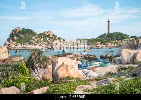 Landschaftlich schöner Blick auf den Leuchtturm an der schönen Küste mit großen Steinen. Blick auf die Bucht mit kristallklarem Wasser. Bunte vietnamesische Fischerboote. Stockfoto