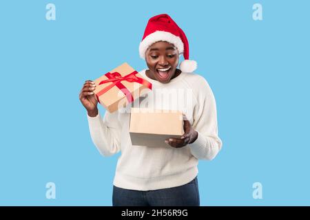 Schwarze Dame Eröffnung Weihnachtsgeschenk Trägt Weihnachtsmütze, Blauer Hintergrund Stockfoto