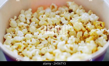 Nahaufnahme der männlichen Hand, die Popcorn aus einem Eimer nimmt, Konzept des Kinos. Mann nimmt süßes, köstliches Popcorn aus einer dunkelblauen Schüssel. Stockfoto
