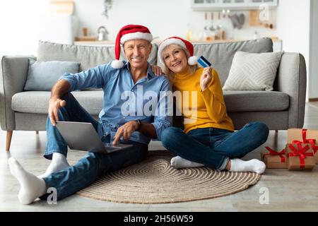 Ehepartner Zeigen Kreditkarte Mit Laptop-Shopping Auf Weihnachten Indoor Stockfoto