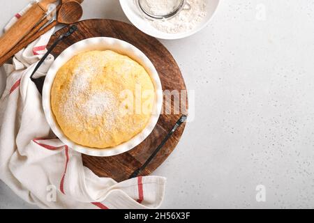 Roher Hefeteig mit Kürbis in weißer Schüssel mit Handtuch auf dem bemehlten Küchentisch bedeckt, Rezeptidee. Konzept Hausbacken Brot, Brötchen oder Cinnabon o Stockfoto