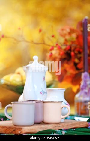 Tassen Tee und großes weißes Glas auf rustikaler Holzbank, Picknick im Herbstwald. Herbstwochenende. Foto getönte, selektive Fokussierung. Stockfoto