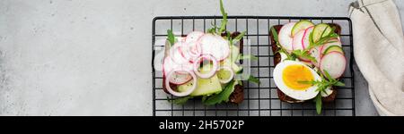 Offene Sandwiches auf dunklem Roggenbrot mit Eiern, Garnelen, Radieschen, Gurken, Frischkäse und Rucola zum Frühstück. Ein traditionelles, smorrebrodtes Danis-Gericht Stockfoto