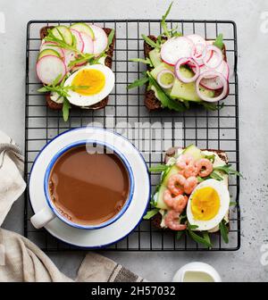 Offene Sandwiches auf dunklem Roggenbrot mit Eiern, Garnelen, Radieschen, Gurken, Frischkäse und Rucola zum Frühstück. Ein traditionelles, smorrebrodtes Danis-Gericht Stockfoto