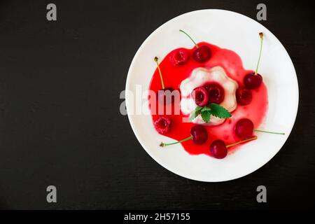 Kokosnussgelee mit Sommerbeeren. Panna Cotta mit süßer Kirsche auf dem Teller. Flach liegend Stockfoto