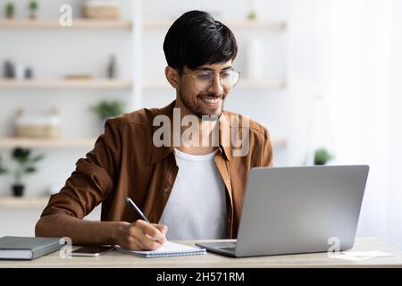 Hübscher arabischer Angestellter, der im Internet surft und sich Notizen gemacht hat Stockfoto