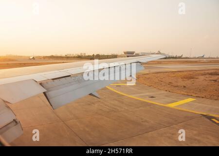 Flügelansicht aus der Kabine des Flugzeugs nach der Landung auf der Start- und Landebahn am Flughafen, orangefarbener Morgensonnenaufgang Stockfoto