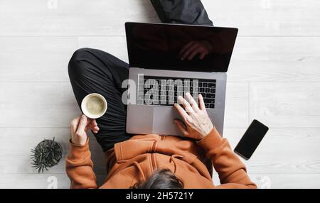Während der Coronavirus-Pandemie arbeitet ein Geschäftsmann zu Hause. Freiberuflicher Mitarbeiter mit Laptop arbeitet, während er auf dem Boden sitzt. Online-Schulungen. Stockfoto