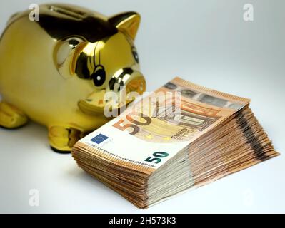 Goldenes Sparschwein mit einem Stapel von 50-Euro-Banknoten im Vordergrund. Stockfoto