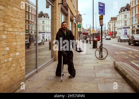 Ein behinderter Mann in der Dalston High Street, der seine Mütze ausstreut und um Geld bittet. Stockfoto