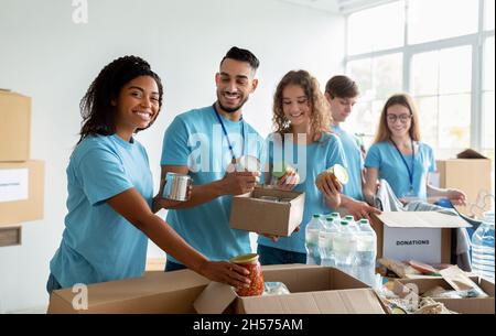 Eine vielfältige Gruppe von Freiwilligen, die gespendete Lebensmittel in Kisten sortieren, in einem gemeinnützigen Spendenzentrum arbeiten und lächeln Stockfoto