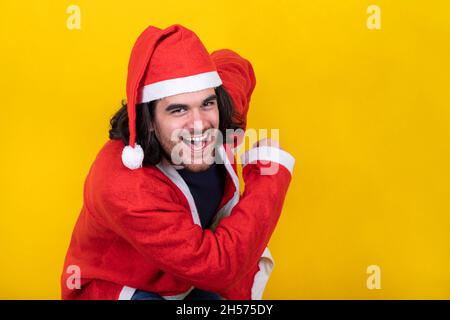 Schöner Mann ist als Weihnachtsmann gekleidet und tanzt glücklich. Der junge Mann lächelt und schaut in die Kamera. Gelber Hintergrund und Kopierbereich. Stockfoto