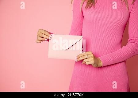 Nahaufnahme einer weiblichen Person, die einen pinkfarbenen Einladungsumschlag mit Geschenkgutschein, Postkarte und Hochzeitseinladungskarte hält Stockfoto