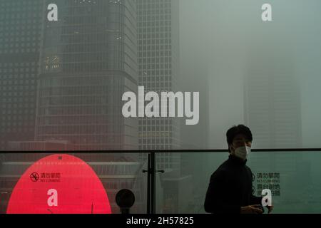 Ein junger Mann fotografiert einen Wolkenkratzer, der in starkem Smog gehüllt ist, im Geschäftszentrum von Peking, China. 06-Nov-2021 Stockfoto